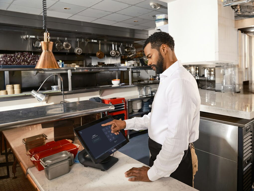 Mitarbeiter in einer Restaurantküche bedient einen Touchscreen mit Bestellungen